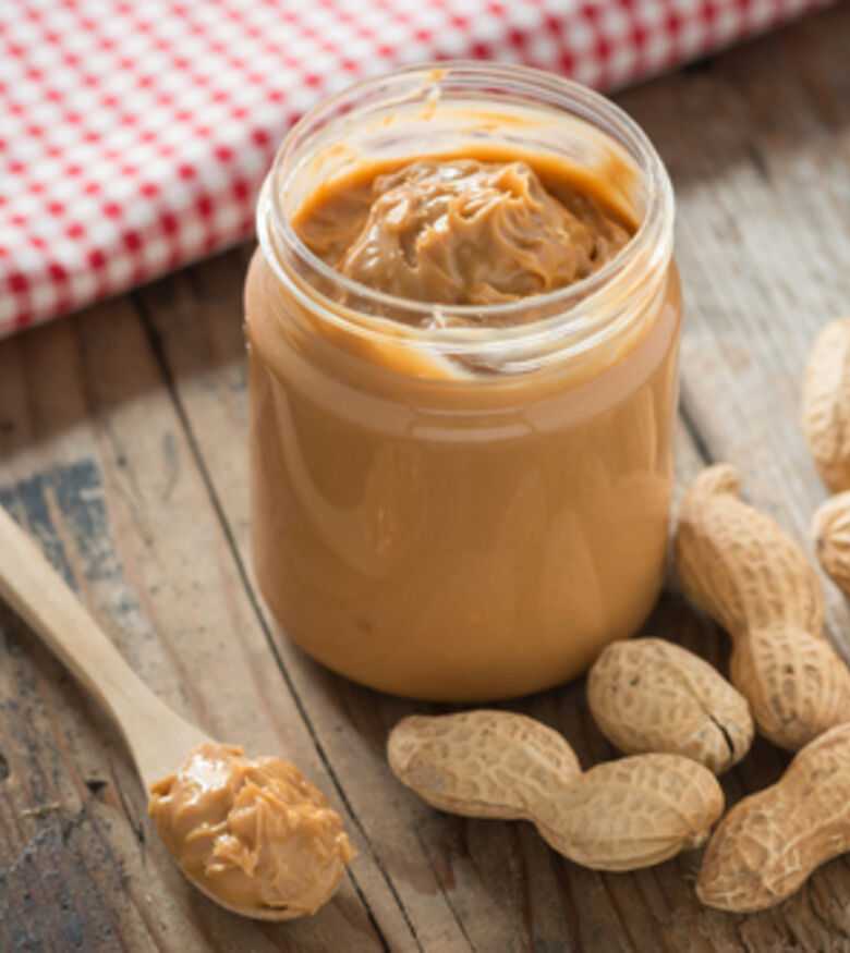 Open jar of creamy peanut butter with whole peanuts and a spreader on a rustic wooden table