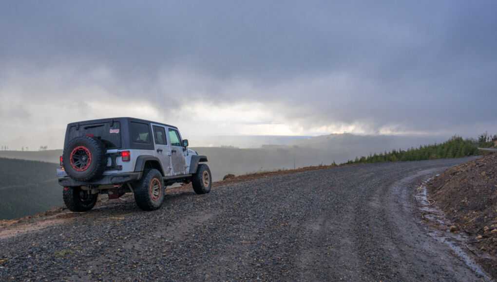 Four-wheel drive SUV on a gravel road in a mountainous area with overcast skies.