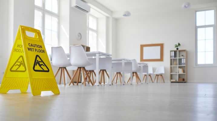 Yellow caution wet floor sign in spacious modern office with large windows and stylish furniture