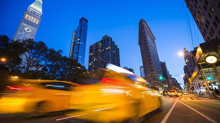 blurred yellow taxi speeding past historic Flatiron Building at dusk in New York City