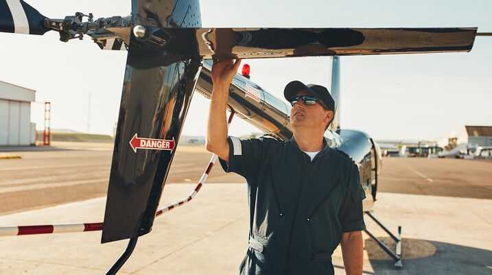 Aviation mechanic performing pre-flight inspection on helicopter tail rotor at airfield during sunset