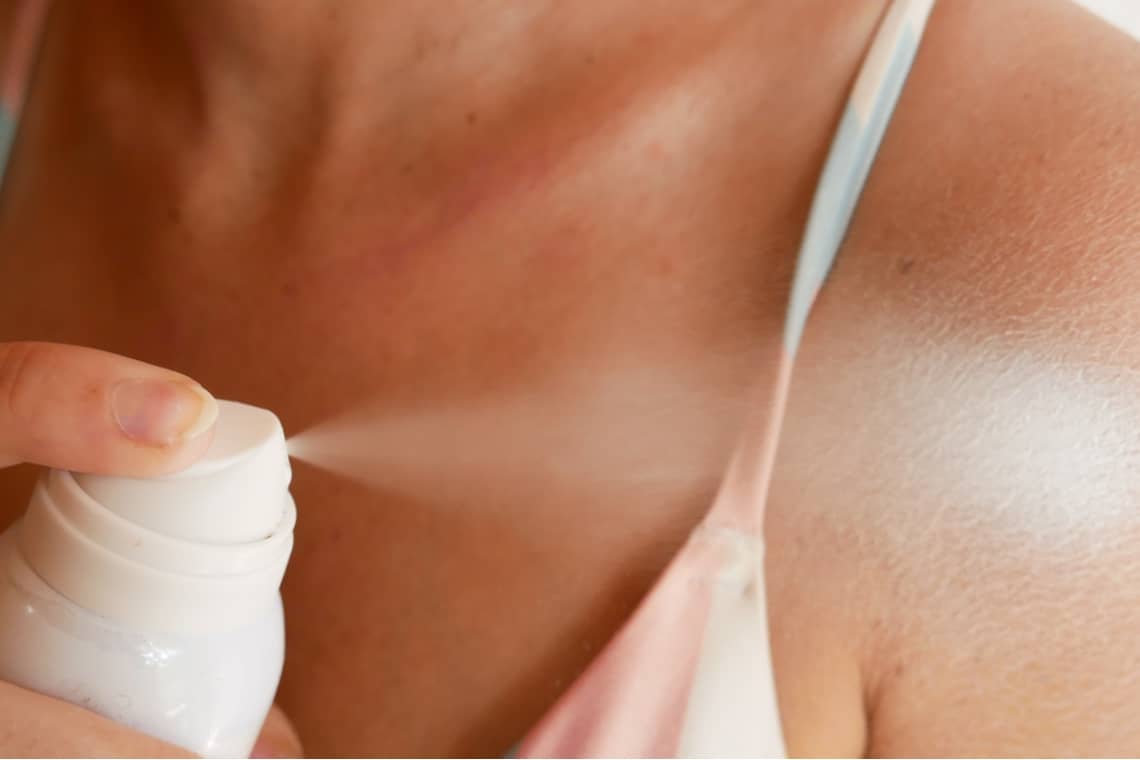 Woman spraying herself sunscreen