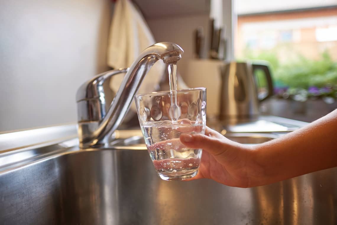 hands pouring glass of fresh water from tap in kitchen
