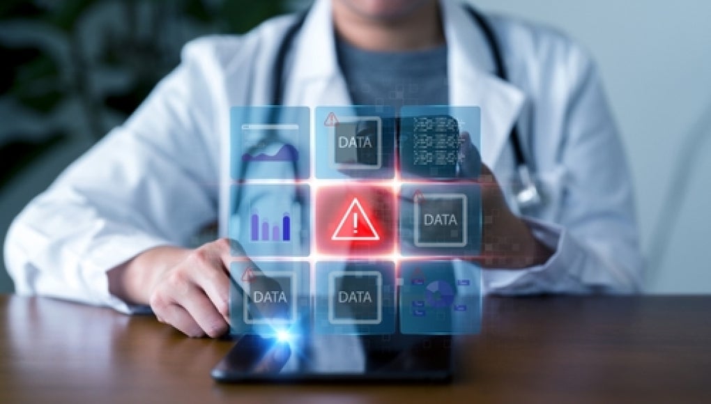 medical professional holding a tablet with data breach warning symbol 
