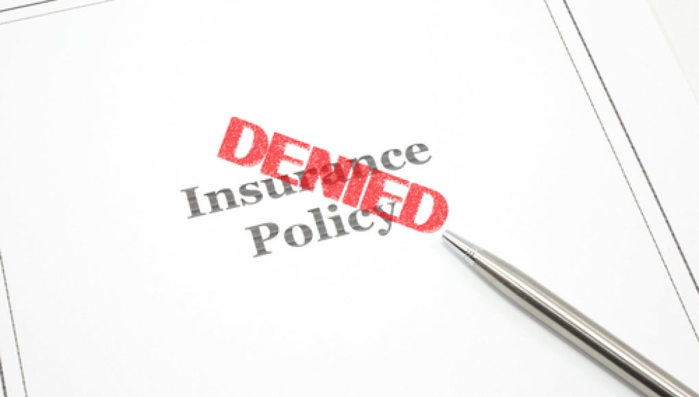 insurance policy paper with pen and red "DENIED" stamp on top of the paper 