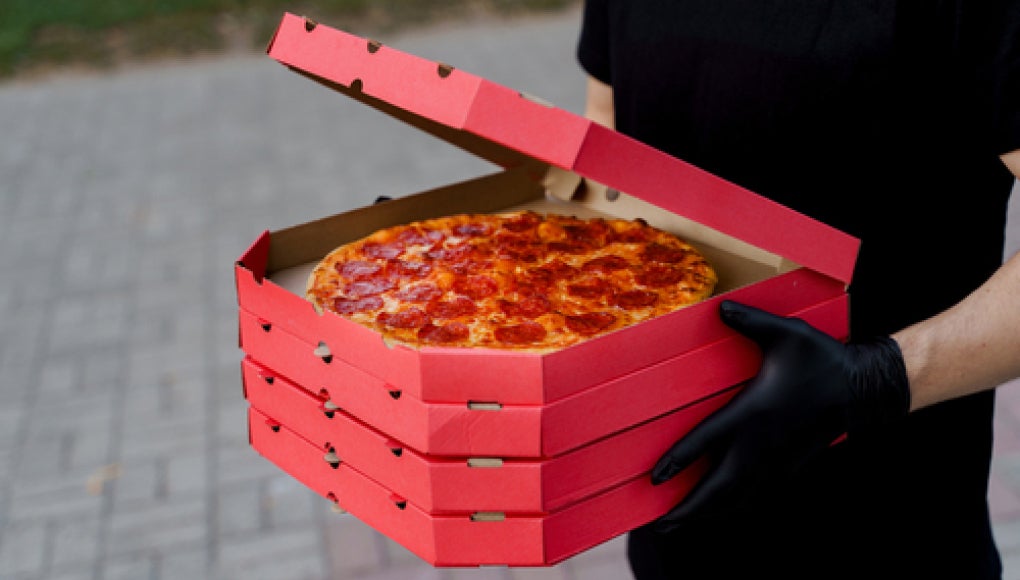 delivery person in all black holding boxes of pizza in their hands.