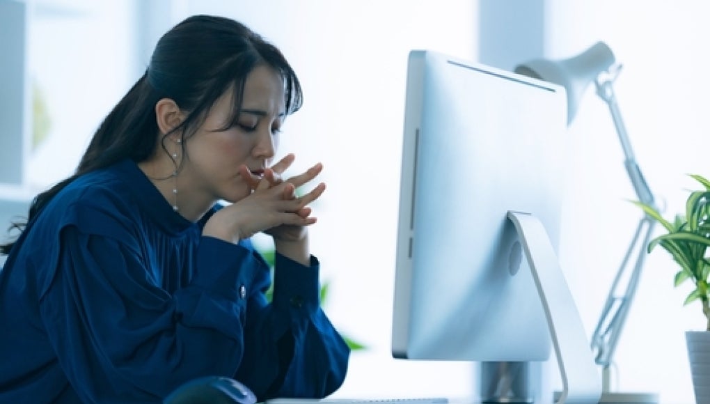woman sitting in front of computer with hands put together, worried