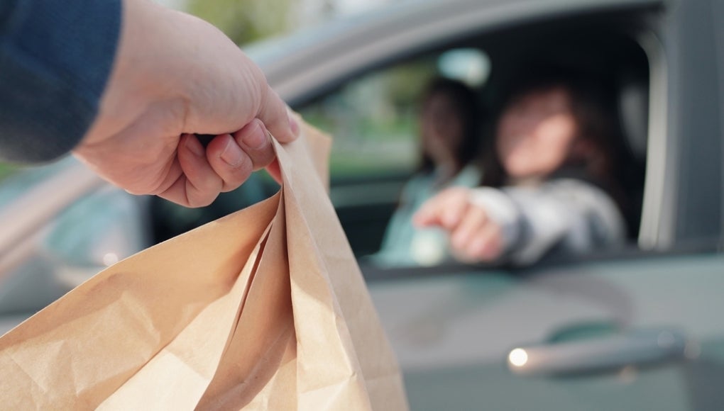 Fast food concept, delivery through auto window. Delicious meal, for travelers by auto. Woman driving, food delivery to car in package. Food for driver, passenger to eat on road. Buying food in car.