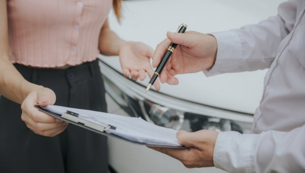 two people reviewing insurance claim with car in background