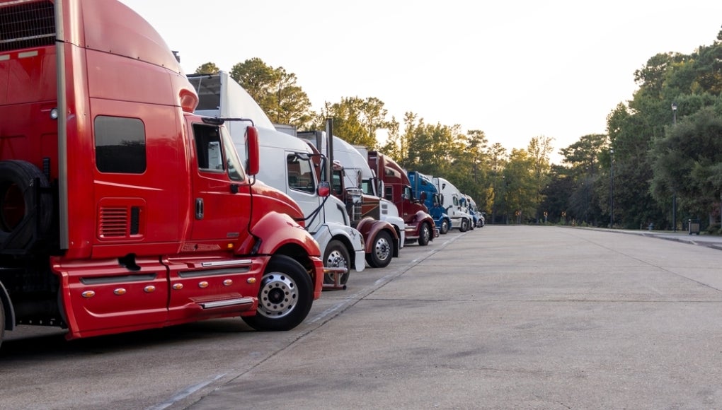 Row of colorful semi trucks lined up at dusk in a truck stop parking area.