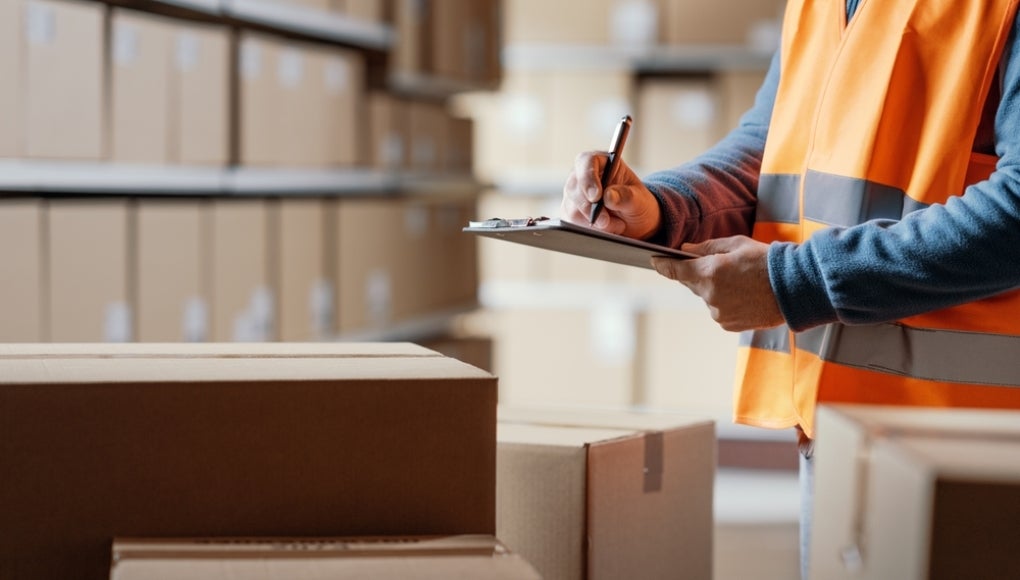 Warehouse operative checking a document on a clipboard and preparing a shipment
