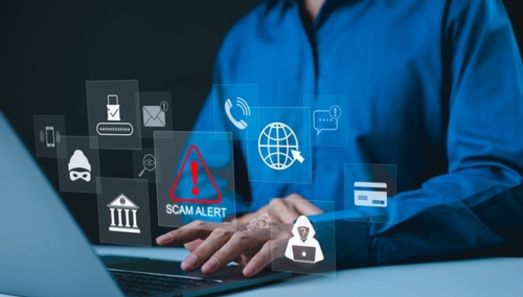 person sitting in front of laptop with a variety of icons with a scam icon in red popping up 