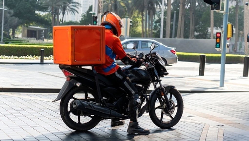 delivery person on a motorbike with a red delivery container on the back 