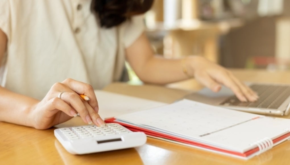 person calculating wages using a calculator and spreadsheet 