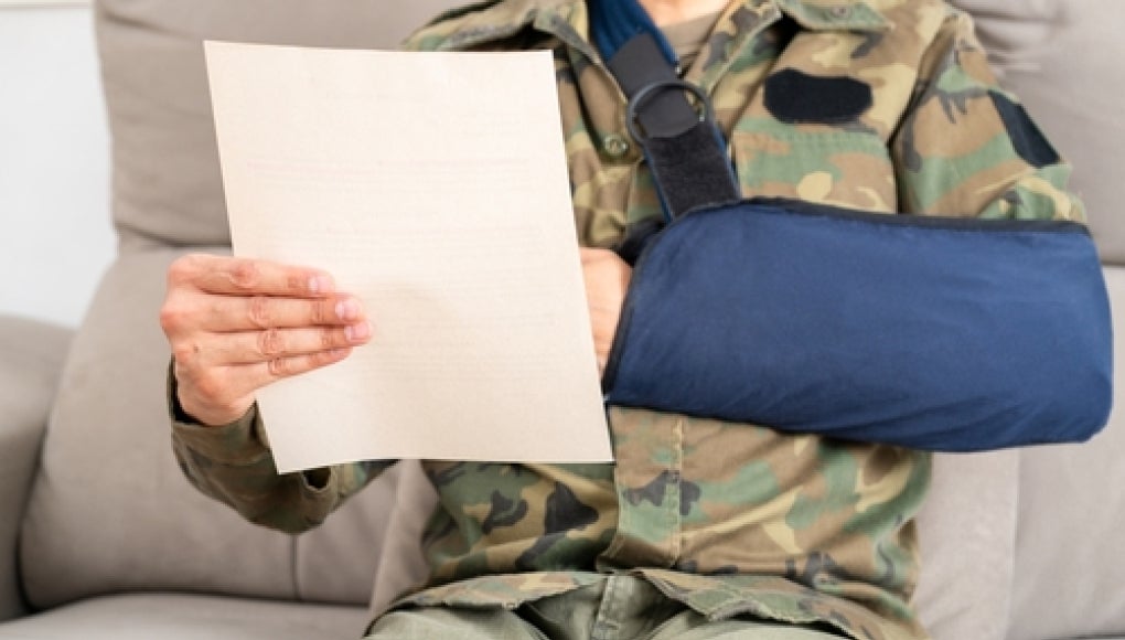 veteran in a arm sling reading a claim paper 