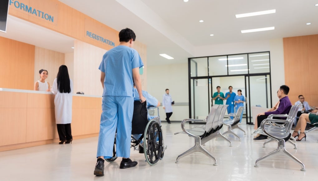 Medical staff and patients in a busy hospital reception services at information desk, atmosphere many patients wait for healthcare specialists in hospital. medical team doctors walking pass lobby