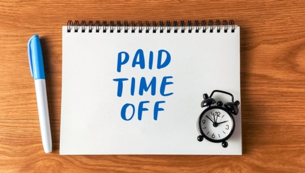 paid time off written on pad of paper with a clock on a desk