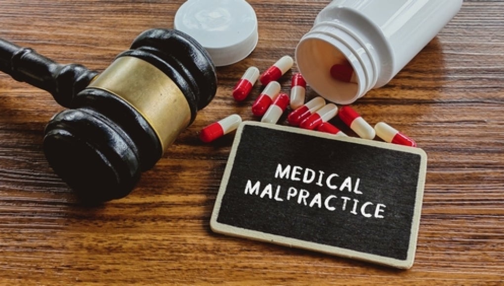 gavel with chalkboard that reads "medical malpractice" with pills nearby. 