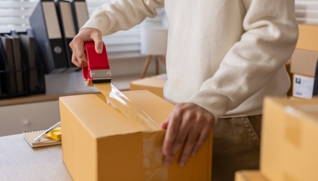 person packing cardboard boxes to ship item. 