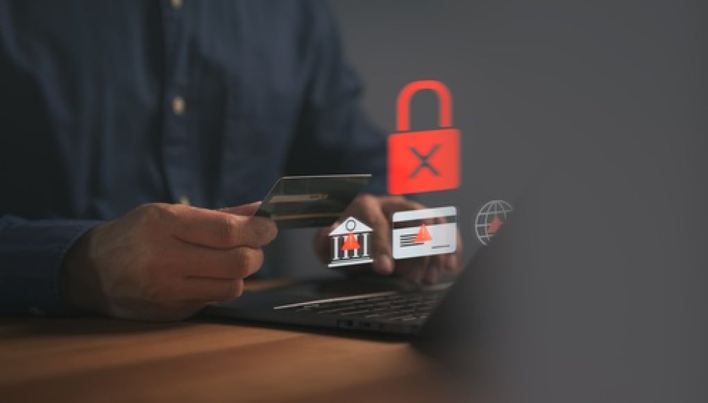 person sitting in front of laptop with error messages, holding a credit card and their phone in hand 