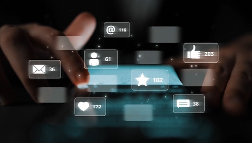 pair of hands scrolling through a phone with various social media icons popping up showing a variety of likes, comments, and other means of communicating via social media and videos. 
