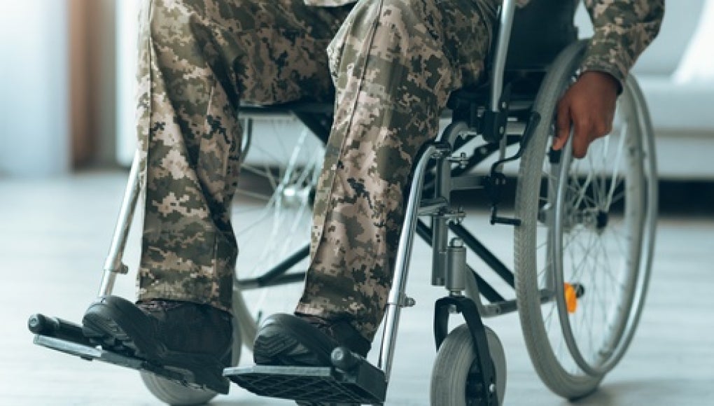 person wearing camoflague sitting in a wheelchair, hands on the wheels 