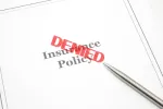 insurance policy paper with pen and red "DENIED" stamp on top of the paper 