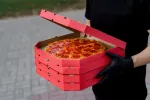 delivery person in all black holding boxes of pizza in their hands.