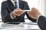 two suited employees exchanging notes, a tablet between them