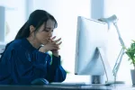 woman sitting in front of computer with hands put together, worried