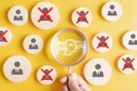 image of a hand holding a magnifying glass with a image of a robot on it, with circles filled with images of peoples being X'd out surrounding it, image has a yellow background