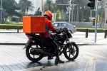delivery person on a motorbike with a red delivery container on the back 