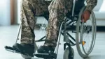 person wearing camoflague sitting in a wheelchair, hands on the wheels