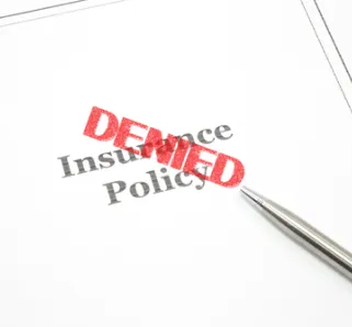 insurance policy paper with pen and red "DENIED" stamp on top of the paper