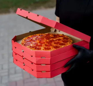 delivery person in all black holding boxes of pizza in their hands.