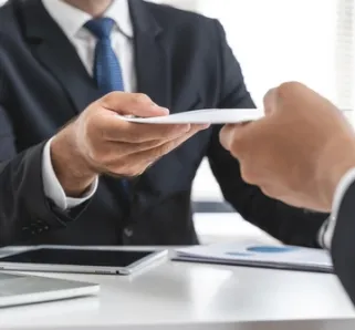 two suited employees exchanging notes, a tablet between them 