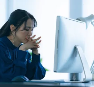 woman sitting in front of computer with hands put together, worried