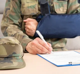 veteran with arm in cast sitting on couch filling out a form on a clipboard with a pen in hand.
