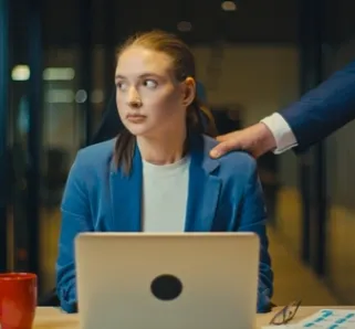 photo of a woman in a suit at work looking away as someone touches her shoulder