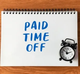 paid time off written on pad of paper with a clock on a desk