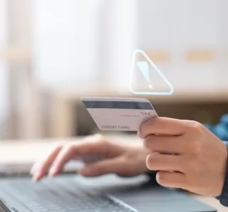 person sitting in front of laptop holding a bank card with a error sign indicating fraud