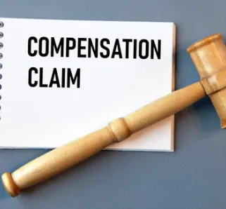 notepad with the words 'compensation claim' on it, with a grey background and wooden gavel resting on top of it 
