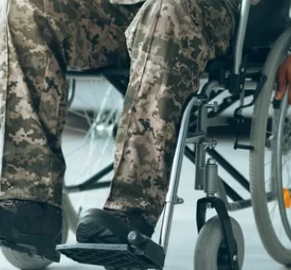 person wearing camoflague sitting in a wheelchair, hands on the wheels