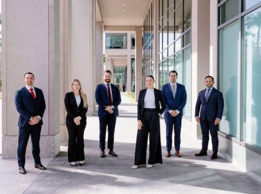 A group of six professionally dressed people stand outside a modern office building.