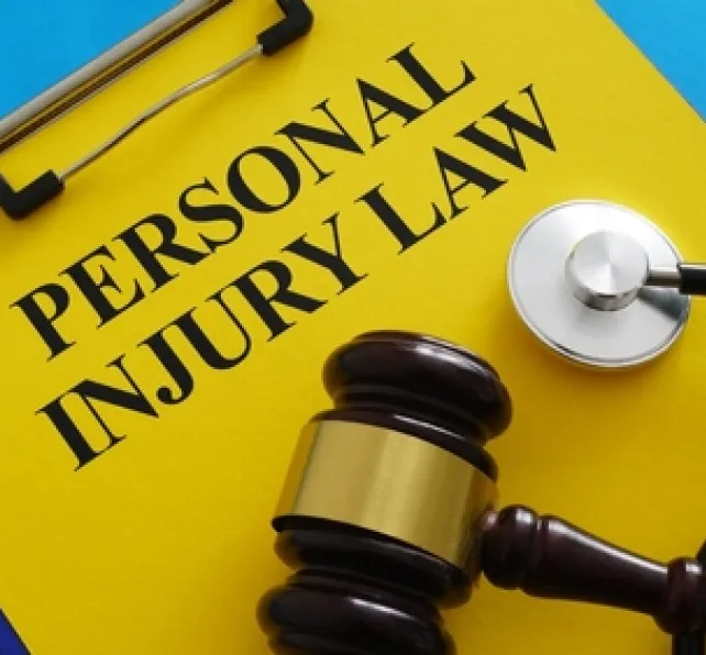 clipboard with yellow paper with the words "Personal Injury Law" on it, with a blue background, there is a stethoscope and gavel resting on top of the clipboard
