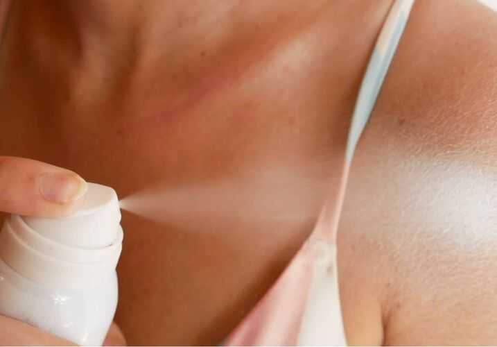 Woman spraying herself sunscreen