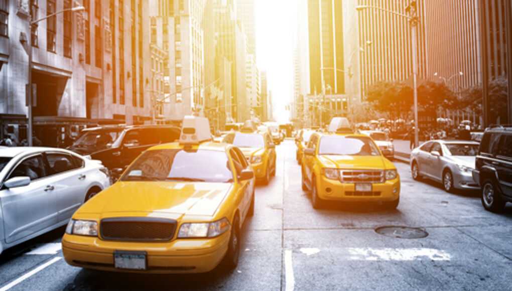 Yellow taxicabs in busy New York City traffic with sunlight flaring down the avenue