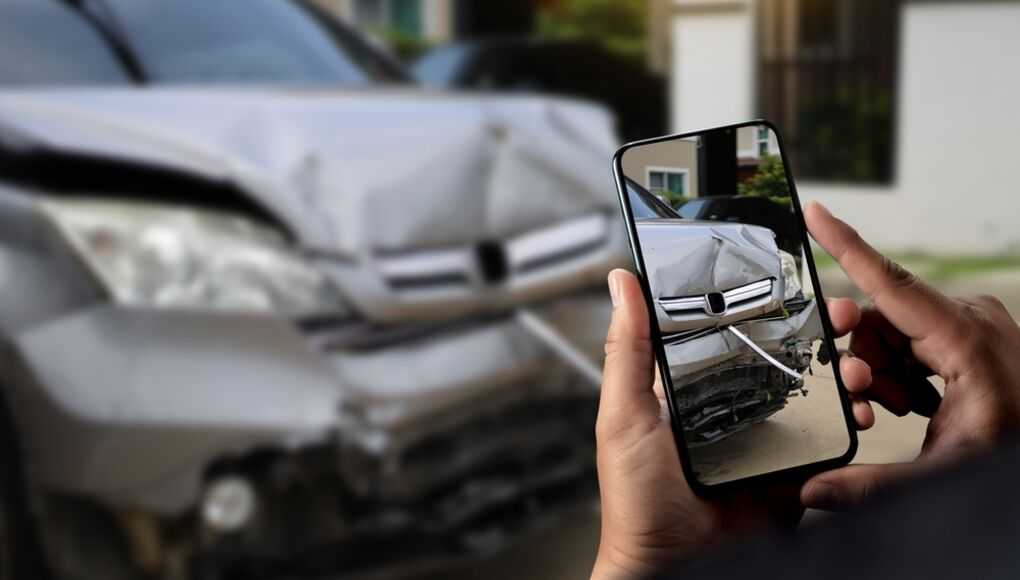 Person using smartphone to photograph front-end damage of a silver car after an accident