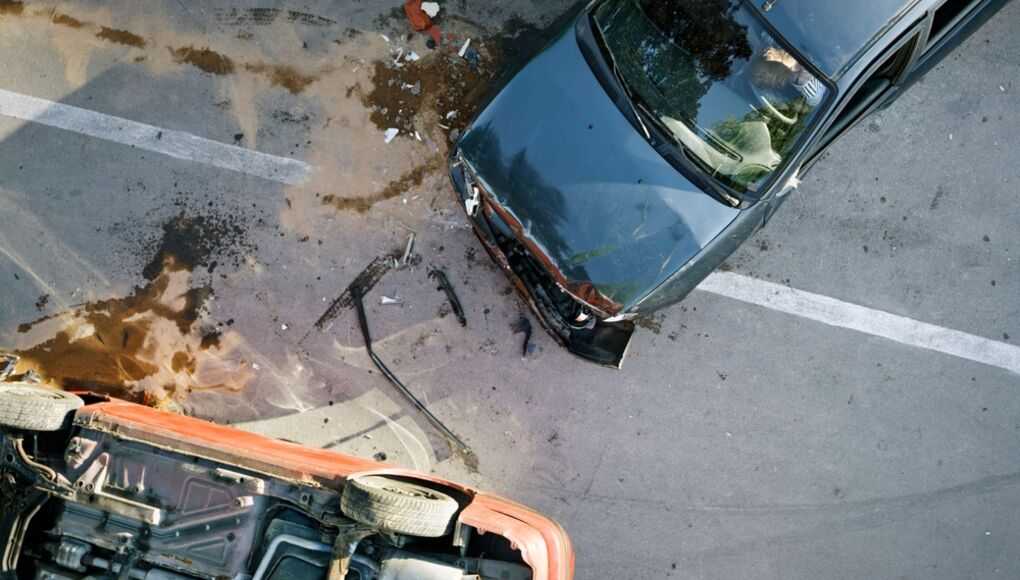 "Aerial view of a car accident with two damaged vehicles on a parking lot, showing debris and oil stains on asphalt.