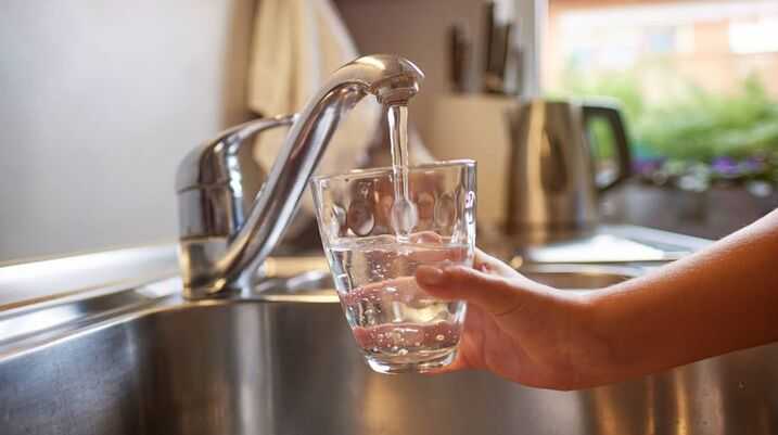 hands pouring glass of fresh water from tap in kitchen
